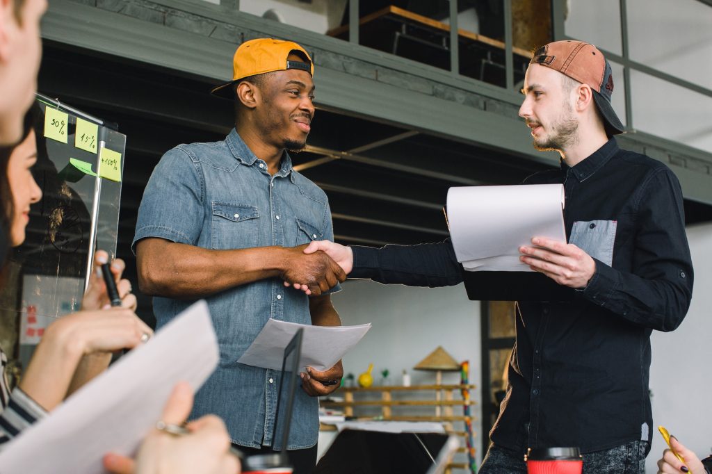 Creative African and Caucasian young men shaking hands during work meeting in office. Team work